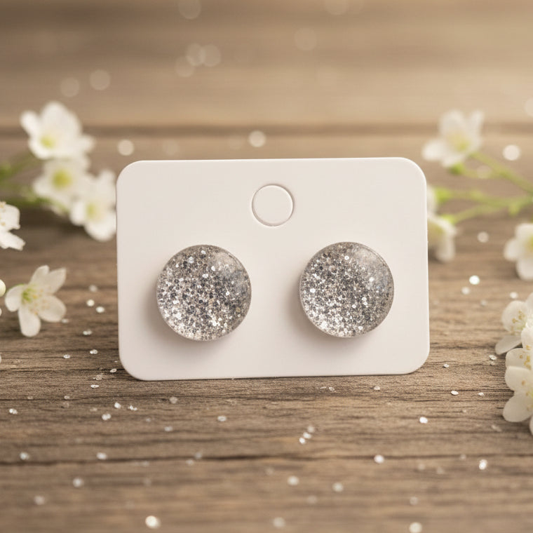 Silver glittery stud earrings on a white card against a wood background