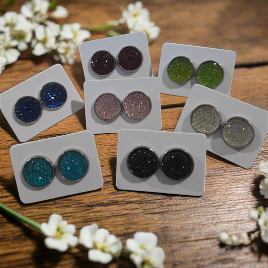 Assorted pairs of glittery earrings on white cards displayed on a wooden surface.
