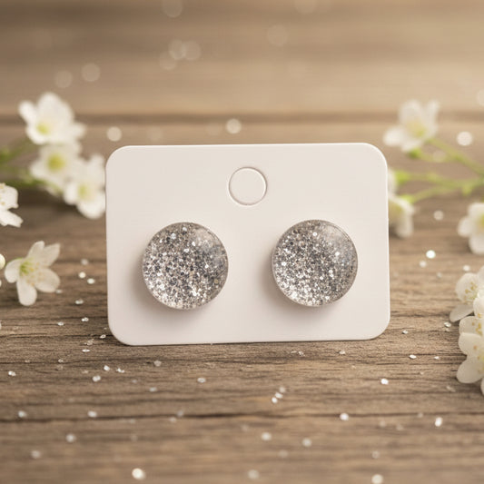 Silver glittery stud earrings on a white card against a wood background